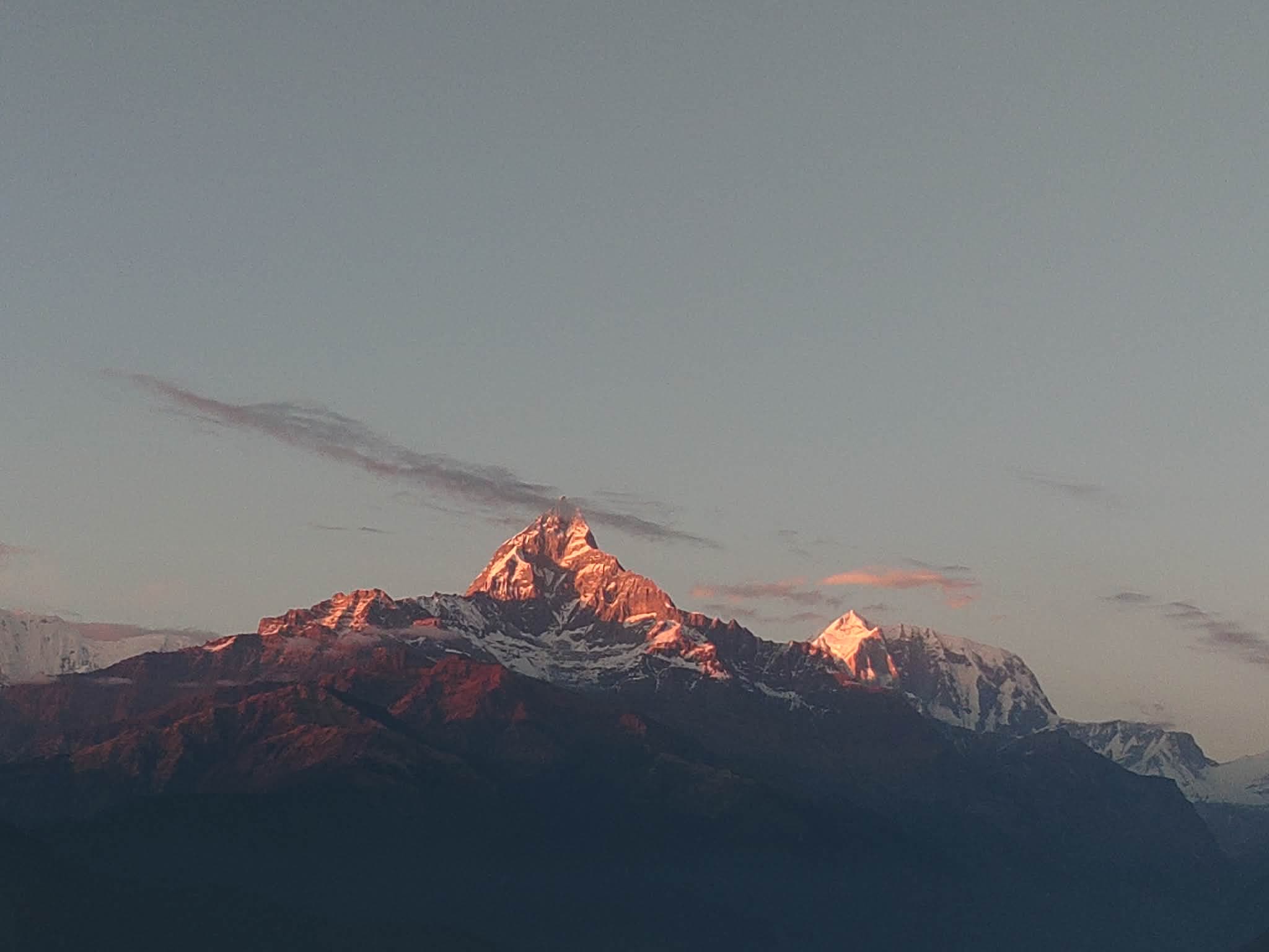 Warm pink light touching a mountain summit above dark ridges.