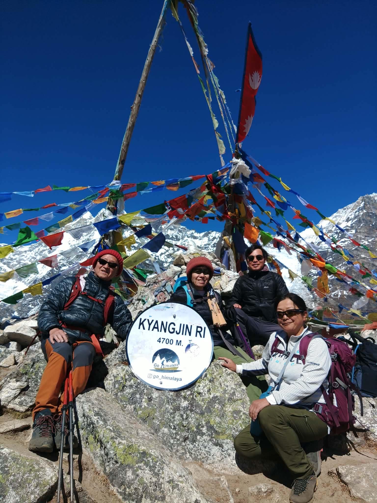 Trekkers gathered beside a viewpoint marker under colourful prayer flags.